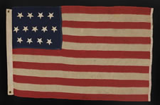 13 HAND-SEWN, UPSIDEDOWN STARS, IN THE 4-5-4 PATTERN, ON AN EXTREMELY SMALL SCALE FLAG WITH ITS CANTON RESTING ON THE "WAR STRIPE", MADE BETWEEN 1864 AND THE 1876 CENTENNIAL OF AMERICAN INDEPENDENCE