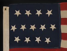 13 HAND-SEWN, UPSIDEDOWN STARS, IN THE 4-5-4 PATTERN, ON AN EXTREMELY SMALL SCALE FLAG WITH ITS CANTON RESTING ON THE "WAR STRIPE", MADE BETWEEN 1864 AND THE 1876 CENTENNIAL OF AMERICAN INDEPENDENCE