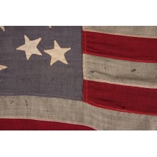 13 STAR FLAG WITH A MEDALLION CONFIGURATION OF HAND-SEWN STARS ON A DUSTY BLUE CANTON; A SMALL-SCALE ANTIQUE AMERICAN FLAG OF THE LATE 19TH CENTURY: