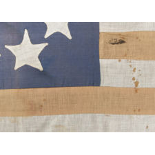 HOMEMADE FLAG WITH 13 STARS ARRANGED IN THE CIRCULAR WREATH PATTERN OFTEN ATTRIBUTED TO BETSY ROSS, WITH ENDEARING WEAR, AND WITH ITS CANTON RESTING ON THE WAR STRIPE, CA 1890-1920's