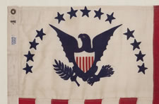 RARE REVENUE CUTTER SERVICE FLAG WITH A BLUE EAGLE AMID AN ARCH OF 13 BLUE STARS ON A WHITE FIELD AND 16 VERTICAL RED AND WHITE STRIPES, CA 1900-1915