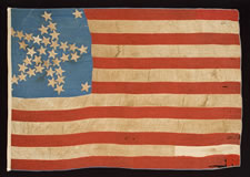 A WELL-LOVED, CARRIED, AND MENDED 36 STAR FLAG THAT PROBABLY STARTED LIFE WITH 33 STARS, ARRANGED IN A "GREAT STAR" PATTERN, CIVIL WAR PERIOD, GREAT SMALL SIZE AND CORNFLOWER BLUE COLOR, 1861-65