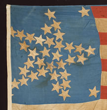 A WELL-LOVED, CARRIED, AND MENDED 36 STAR FLAG THAT PROBABLY STARTED LIFE WITH 33 STARS, ARRANGED IN A "GREAT STAR" PATTERN, CIVIL WAR PERIOD, GREAT SMALL SIZE AND CORNFLOWER BLUE COLOR, 1861-65