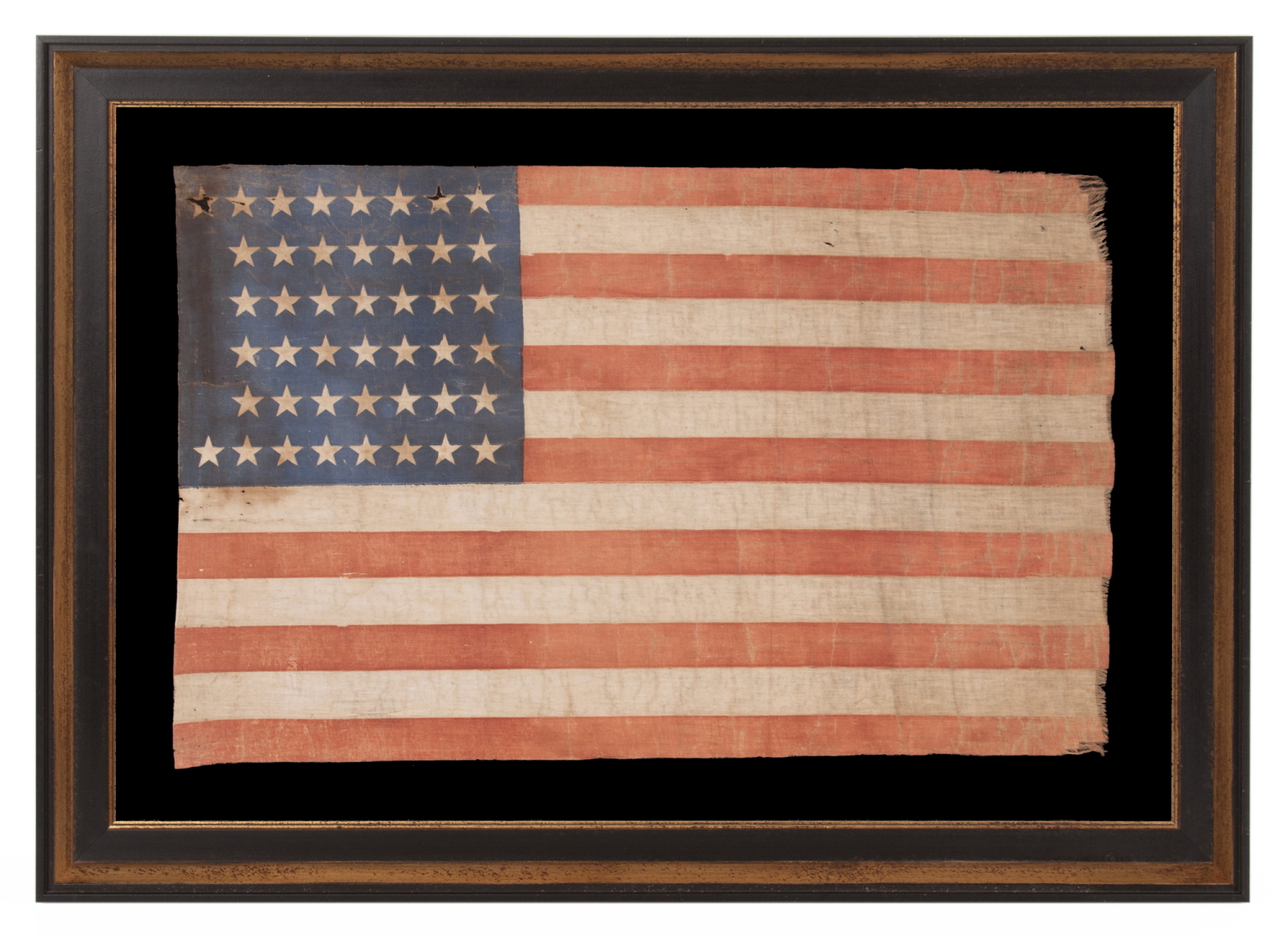 44 STAR ANTIQUE AMERICAN PARADE FLAG WITH ENDEARING WEAR FROM LONG TERM USE AND WITH ITS STARS ARRANGED IN A NOTCHED PATTERN THAT LEAVES 4 SPACES OPEN FOR THE REMAINING WESTERN TERRITORIES, REFLECTS THE PERIOD WHEN WYOMING WAS THE MOST RECENT STATE TO JOIN THE UNION, 1890-1896