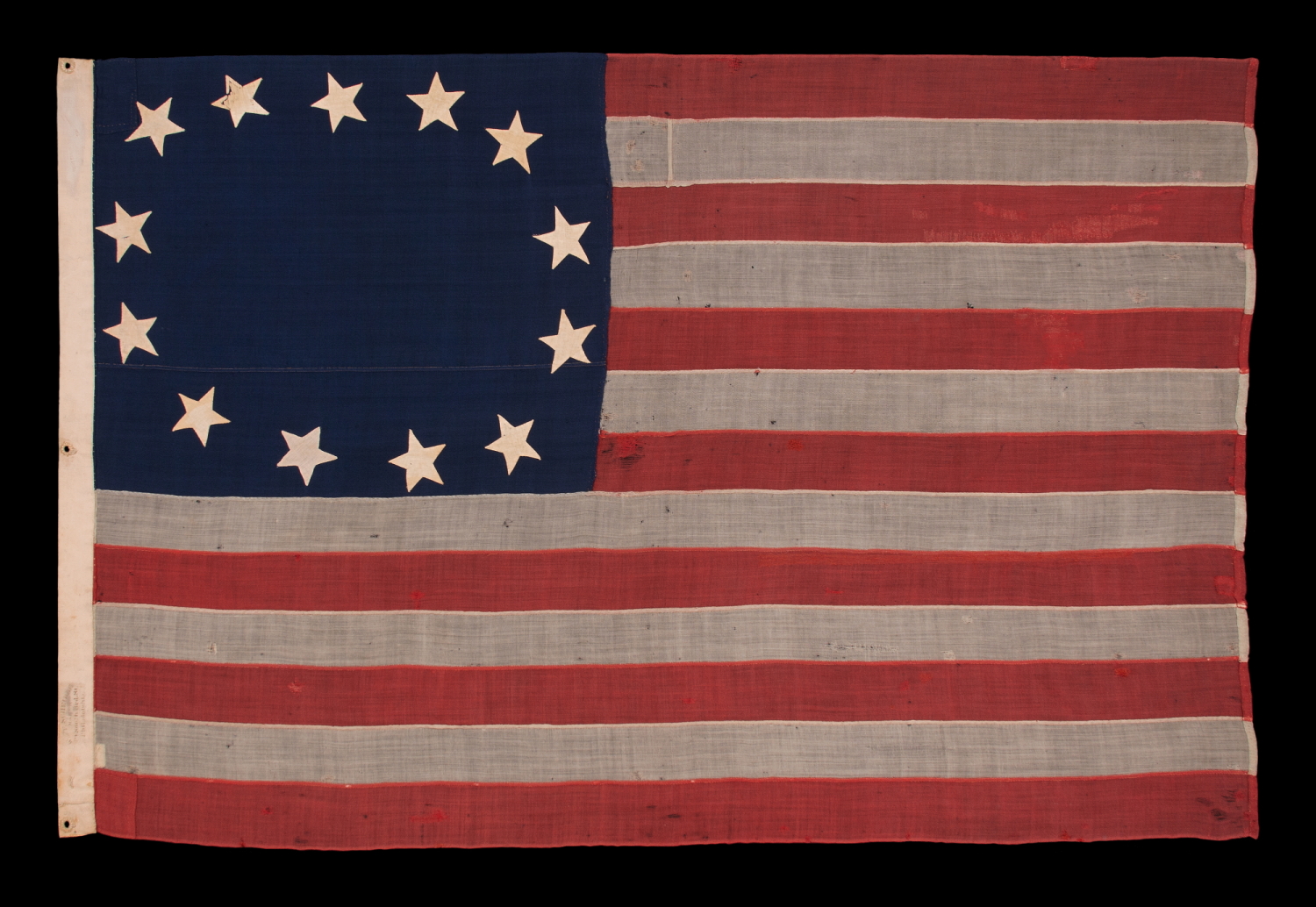 13 STARS IN A CRUDE SINGLE WREATH, REMINISCENT OF THE BETSY ROSS PATTERN, THOUGH RENDERED AS MORE OF AN OVAL; ON AN ANTIQUE AMERICAN FLAG MADE & SIGNED BY THE SHOP OF WILLIAM SCHEIBLE, 49 S. 3RD STREET, PHILADELPHIA, APPROX. TWO BLOCKS FROM INDEPENDENCE HALL AND THE SAME FROM THE BETSY ROSS HOUSE; A CIVIL WAR ERA FLAG, WITH AN EXTREMELY RARE & DESIRABLE CONFIGURATION OF STARS FOR THIS PERIOD, CIRCA 1861-65