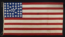 39 STARS IN A LINEAL PATTERN WITH A HUGE, HALOED CENTER STAR AND DYNAMIC VISUAL FEATURES, ITS CANTON RESTING ON THE WAR STRIPE, PROBABLY MADE FOR THE 1876 CENTENNIAL OF AMERICAN INDEPENDENCE, NEVER AN OFFICIAL STAR COUNT, REFLECTS THE ANTICIPATED ARRIVAL OF COLORADO AND THE DAKOTA TERRITORY