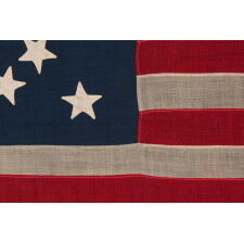 13 STAR ANTIQUE AMERICAN FLAG WITH A MEDALLION CONFIGURATION OF HAND-SEWN STARS AND A BEAUTIFUL, ELONGATED PROFILE, MADE IN THE ERA OF THE 1876 CENTENNIAL OF AMERICAN INDEPENDENCE, IN AN UNCOMMONLY SMALL SIZE AMONG ITS COUNTERPARTS OF THE PERIOD WITH SEWN CONSTRUCTION