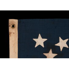 13 STAR ANTIQUE AMERICAN FLAG WITH A MEDALLION CONFIGURATION OF HAND-SEWN STARS AND A BEAUTIFUL, ELONGATED PROFILE, MADE IN THE ERA OF THE 1876 CENTENNIAL OF AMERICAN INDEPENDENCE, IN AN UNCOMMONLY SMALL SIZE AMONG ITS COUNTERPARTS OF THE PERIOD WITH SEWN CONSTRUCTION