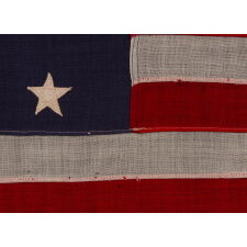 13 STAR ANTIQUE AMERICAN FLAG WITH A 3-2-3-2-3 CONFIGURATION OF STARS ON AN ATTRACTIVE, INDIGO BLUE CANTON; A SMALL-SCALE EXAMPLE OF THE 1895-1926 ERA, INSCRIBED WITH THE SURNAME “SPENGE,” LIKELY PRODUCED BY A MAKER WITH LINKS TO THE U.S. ARMY’S 19th CORPS