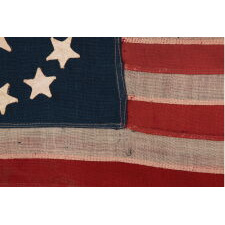 13 STAR ANTIQUE AMERICAN FLAG, IN A TINY SCALE AMONG PIECED-AND-SEWN EXAMPLES OF THE 19TH CENTURY, WITH HAND-SEWN STARS ARRANGED IN A CIRCULAR VERSION OF WHAT IS KNOWN AS THE 3RD MARYLAND PATTERN; FEATURES AN ESPECIALLY LARGE CENTER STAR, MADE circa 1885-1895