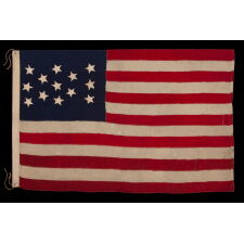 13 STAR ANTIQUE AMERICAN FLAG WITH HAND-SEWN STARS IN AN EXTREMELY NARROW PRESENTATION OF A 3-2-3-2-3 ARRANGEMENT ON A CANTON THAT DOESN’T FOLLOW SUIT, LEAVING WIDE EXPANSES OF BLUE WOOL BUNTING ABOVE AND BELOW; MADE IN THE ERA OF THE 1876 CENTENNIAL OF AMERICAN INDEPENDENCE, POSSIBLY AS A U.S. NAVY SMALL BOAT ENSIGN