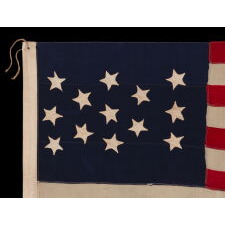 13 STAR ANTIQUE AMERICAN FLAG WITH HAND-SEWN STARS IN AN EXTREMELY NARROW PRESENTATION OF A 3-2-3-2-3 ARRANGEMENT ON A CANTON THAT DOESN’T FOLLOW SUIT, LEAVING WIDE EXPANSES OF BLUE WOOL BUNTING ABOVE AND BELOW; MADE IN THE ERA OF THE 1876 CENTENNIAL OF AMERICAN INDEPENDENCE, POSSIBLY AS A U.S. NAVY SMALL BOAT ENSIGN