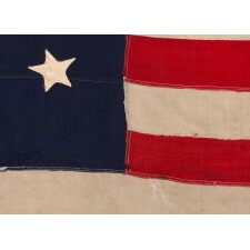 13 STAR ANTIQUE AMERICAN FLAG WITH HAND-SEWN STARS IN AN EXTREMELY NARROW PRESENTATION OF A 3-2-3-2-3 ARRANGEMENT ON A CANTON THAT DOESN’T FOLLOW SUIT, LEAVING WIDE EXPANSES OF BLUE WOOL BUNTING ABOVE AND BELOW; MADE IN THE ERA OF THE 1876 CENTENNIAL OF AMERICAN INDEPENDENCE, POSSIBLY AS A U.S. NAVY SMALL BOAT ENSIGN