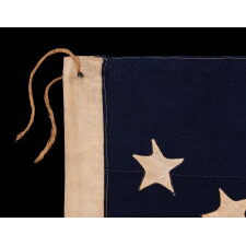 13 STAR ANTIQUE AMERICAN FLAG WITH HAND-SEWN STARS IN AN EXTREMELY NARROW PRESENTATION OF A 3-2-3-2-3 ARRANGEMENT ON A CANTON THAT DOESN’T FOLLOW SUIT, LEAVING WIDE EXPANSES OF BLUE WOOL BUNTING ABOVE AND BELOW; MADE IN THE ERA OF THE 1876 CENTENNIAL OF AMERICAN INDEPENDENCE, POSSIBLY AS A U.S. NAVY SMALL BOAT ENSIGN