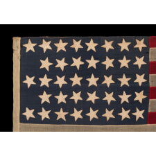38 STAR ANTIQUE AMERICAN FLAG IN A TINY SCALE AMONG THOSE WITH PIECED-AND-SEWN CONSTRUCTION, WITH A BEAUTIFUL & UNUSUAL SHADE OF BLUE AND WITH A NOTCHED CONFIGURATION OF STARS THAT LEAVES ROOM FOR WESTERN TERRITORIES THAT HAD YET TO BE ADDED; REFLECTS THE PERIOD WHEN COLORADO WAS THE MOST RECENT STATE TO JOIN THE UNION, 1876-1889