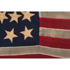 ANTIQUE AMERICAN FLAG WITH A WHIMSICAL PRESENTATION OF 13 STARS IN THE 4-5-4 PATTERN, A VERY EARLY EXAMPLE, MADE circa 1835-1850’s, BOLDY GRAPHIC, ENTIRELY HAND-SEWN AND IN A TINY SCALE AMONG ITS COUNTERPARTS, PROBABLY A U.S. NAVY SMALL BOAT ENSIGN