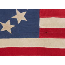 13 STAR ANTIQUE AMERICAN FLAG, MADE OF FINE SILK, WITH AN OVAL VERSION OF WHAT IS KNOWN AS THE 3RD MARYLAND PATTERN AND A LARGE CENTER STAR, IN AN EXTRAORDINARILY TINY SIZE AMONG FLAGS WITH SEWN CONSTRUCTION; FOUND IN WESTERN MASSACHUSETTS, MADE SOMETIME BETWEEN THE 1850’s AND THE CIVIL WAR (1861-65), LIKELY FOR A MILITIA OR VOLUNTEER UNIT, OR AN OFFICER THEREOF; ILLUSTRATED IN “THE STARS & THE STRIPES: FABRIC OF THE AMERICAN SPIRIT” BY RICHARD PIERCE, 2005