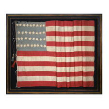34 STAR ANTIQUE AMERICAN FLAG, MADE DURING THE OPENING TWO YEARS OF THE CIVIL WAR, 1861-1863, WITH AN UNUSUALLY ELONGATED FORMAT, A SQUARE CANTON WITH AN ATTRACTIVE SHADE OF BLUE, LARGE, MAKE-DO TASSELS, AND WITH ITS CANTON RESTING ON A RED STRIPE – SOMETIMES TERMED THE ‘BLOOD’ OR THE ‘WAR’ STRIPE; REFLECTS THE PERIOD WHEN KANSAS WAS THE MOST RECENT STATE TO JOIN THE UNION