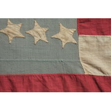 34 STAR ANTIQUE AMERICAN FLAG, MADE DURING THE OPENING TWO YEARS OF THE CIVIL WAR, 1861-1863, WITH AN UNUSUALLY ELONGATED FORMAT, A SQUARE CANTON WITH AN ATTRACTIVE SHADE OF BLUE, LARGE, MAKE-DO TASSELS, AND WITH ITS CANTON RESTING ON A RED STRIPE – SOMETIMES TERMED THE ‘BLOOD’ OR THE ‘WAR’ STRIPE; REFLECTS THE PERIOD WHEN KANSAS WAS THE MOST RECENT STATE TO JOIN THE UNION
