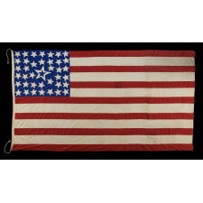 39 STARS ON A HOMEMADE, ANTIQUE AMERICAN FLAG WITH AN EXTREMELY RARE COMBINATION OF JUSTIFIED COLUMNS AND A HUGE, HALOED CENTER STAR, INFUSED AMONG THEM, WITH EXTRAORDINARY COLORS, EXCEPTIONAL VISUAL IMPACT, AND ITS CANTON RESTING ON THE WAR STRIPE; AN UNOFFICIAL STAR COUNT, REFLECT THE ANTICIPATED ARRIVAL OF COLORADO AND THE DAKOTA TERRITORY; LIKELY MADE FOR THE 1876 CENTENNIAL OF AMERICAN INDEPENDENCE