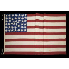 39 STARS ON A HOMEMADE, ANTIQUE AMERICAN FLAG WITH AN EXTREMELY RARE COMBINATION OF JUSTIFIED COLUMNS AND A HUGE, HALOED CENTER STAR, INFUSED AMONG THEM, WITH EXTRAORDINARY COLORS, EXCEPTIONAL VISUAL IMPACT, AND ITS CANTON RESTING ON THE WAR STRIPE; AN UNOFFICIAL STAR COUNT, REFLECT THE ANTICIPATED ARRIVAL OF COLORADO AND THE DAKOTA TERRITORY; LIKELY MADE FOR THE 1876 CENTENNIAL OF AMERICAN INDEPENDENCE