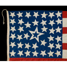 39 STARS ON A HOMEMADE, ANTIQUE AMERICAN FLAG WITH AN EXTREMELY RARE COMBINATION OF JUSTIFIED COLUMNS AND A HUGE, HALOED CENTER STAR, INFUSED AMONG THEM, WITH EXTRAORDINARY COLORS, EXCEPTIONAL VISUAL IMPACT, AND ITS CANTON RESTING ON THE WAR STRIPE; AN UNOFFICIAL STAR COUNT, REFLECT THE ANTICIPATED ARRIVAL OF COLORADO AND THE DAKOTA TERRITORY; LIKELY MADE FOR THE 1876 CENTENNIAL OF AMERICAN INDEPENDENCE