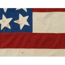 39 STARS ON A HOMEMADE, ANTIQUE AMERICAN FLAG WITH AN EXTREMELY RARE COMBINATION OF JUSTIFIED COLUMNS AND A HUGE, HALOED CENTER STAR, INFUSED AMONG THEM, WITH EXTRAORDINARY COLORS, EXCEPTIONAL VISUAL IMPACT, AND ITS CANTON RESTING ON THE WAR STRIPE; AN UNOFFICIAL STAR COUNT, REFLECT THE ANTICIPATED ARRIVAL OF COLORADO AND THE DAKOTA TERRITORY; LIKELY MADE FOR THE 1876 CENTENNIAL OF AMERICAN INDEPENDENCE