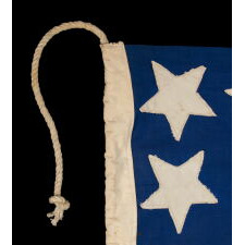 39 STARS ON A HOMEMADE, ANTIQUE AMERICAN FLAG WITH AN EXTREMELY RARE COMBINATION OF JUSTIFIED COLUMNS AND A HUGE, HALOED CENTER STAR, INFUSED AMONG THEM, WITH EXTRAORDINARY COLORS, EXCEPTIONAL VISUAL IMPACT, AND ITS CANTON RESTING ON THE WAR STRIPE; AN UNOFFICIAL STAR COUNT, REFLECT THE ANTICIPATED ARRIVAL OF COLORADO AND THE DAKOTA TERRITORY; LIKELY MADE FOR THE 1876 CENTENNIAL OF AMERICAN INDEPENDENCE