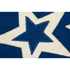 39 STARS ON A HOMEMADE, ANTIQUE AMERICAN FLAG WITH AN EXTREMELY RARE COMBINATION OF JUSTIFIED COLUMNS AND A HUGE, HALOED CENTER STAR, INFUSED AMONG THEM, WITH EXTRAORDINARY COLORS, EXCEPTIONAL VISUAL IMPACT, AND ITS CANTON RESTING ON THE WAR STRIPE; AN UNOFFICIAL STAR COUNT, REFLECT THE ANTICIPATED ARRIVAL OF COLORADO AND THE DAKOTA TERRITORY; LIKELY MADE FOR THE 1876 CENTENNIAL OF AMERICAN INDEPENDENCE