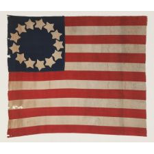 HOMEMADE 13 STAR FLAG OF THE LATE 1890's -1920's ERA, WITH WONDERFULLY FOLKY STARS THAT PRACTICALLY TOUCH ONE-ANOTHER, ARRANGED IN CIRCULAR WREATH PATTERN OFTEN ATTRIBUTED TO BETSY ROSS, AND ITS CANTON RESTING ON THE WAR STRIPE; POSSIBLY MADE DURING WWI (
