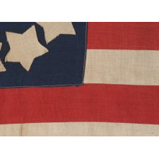 HOMEMADE 13 STAR FLAG OF THE LATE 1890's -1920's ERA, WITH WONDERFULLY FOLKY STARS THAT PRACTICALLY TOUCH ONE-ANOTHER, ARRANGED IN CIRCULAR WREATH PATTERN OFTEN ATTRIBUTED TO BETSY ROSS, AND ITS CANTON RESTING ON THE WAR STRIPE; POSSIBLY MADE DURING WWI (