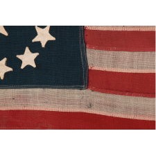 13 STAR ANTIQUE AMERICAN FLAG, IN A TINY SCALE AMONG PIECED-AND-SEWN EXAMPLES OF THE 19TH CENTURY, WITH HAND-SEWN STARS ARRANGED IN A CIRCULAR VERSION OF WHAT IS KNOWN AS THE 3RD MARYLAND PATTERN; FEATURES AN ESPECIALLY LARGE CENTER STAR, MADE circa 1890