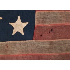 13 STAR ANTIQUE AMERICAN FLAG WITH A MEDALLION CONFIGURATION OF HAND-SEWN STARS AND EXCEPTIONALLY ENDEARING GRAPHIC QUALITIES FROM HAVING BEEN EXTENSIVELY FLOWN; A SMALL SCALE EXAMPLE, MADE IN THE ERA OF THE 1876 CENTENNIAL OF AMERICAN INDEPENDENCE