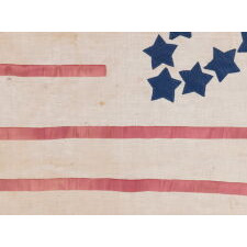 31 STARS IN A GREAT STAR PATTERN, ON AN ANTIQUE AMERICAN FLAG MADE DURING THE PERIOD OF CALIFORNIA STATEHOOD (1850-1858), WITH APPLIQUÉD TEXT ADDED TO CELEBRATE INDEPENDENCE DAY, 1858, THE PRECISE DAY THAT A 32nd STAR WAS OFFICIALLY ADDED FOR MINNESOTA; A MAKE-DO EXAMPLE WITH RIBBON AS STRIPES & EXCEPTIONAL FOLK QUALITIES, CLOSELY RELATED TO FLAGS FOUND IN THE FORMER MAINE HOME OF CPL. JOHN WILLIAM MORIN, WHO FOUGHT WITH THE 20th MAINE REGIMENT UNDER COL. JOSHUA CHAMBERLIN AT GETTYSBURG