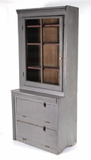 NARROW, MAKE-DO PENNSYLVANIA CUPBOARD IN OLD GREY PAINT OVER AN EARLIER RED, WITH A GLAZED DOOR AND TWO UNUSUAL DROP-DOWN DOORS, CA 1890